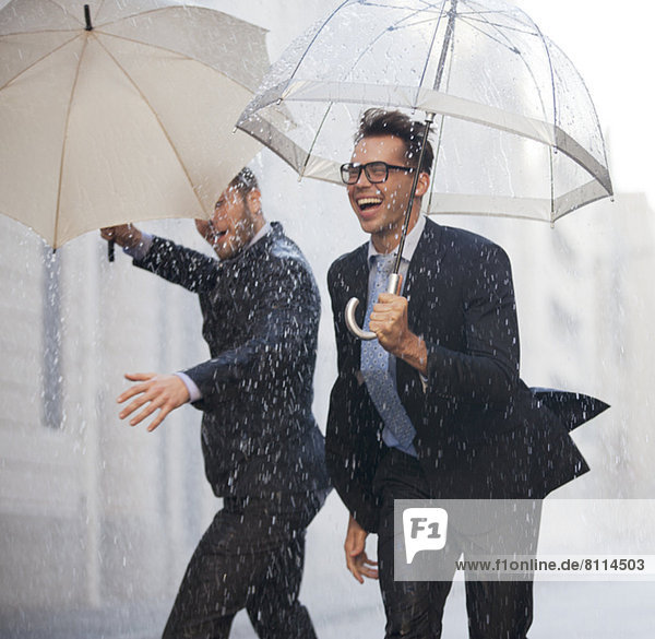 Happy businessmen with umbrellas walking in rain