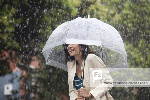Glückliche Frau unter Schirm im Regen