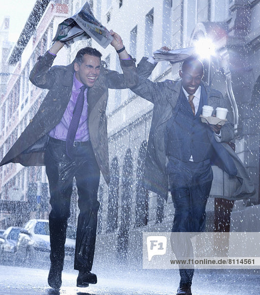 Businessmen carrying coffee and covering heads with newspaper in rain