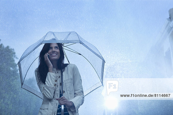 Businesswoman talking on cell phone under umbrella in rain