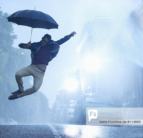Enthusiastic man with umbrella jumping in rain