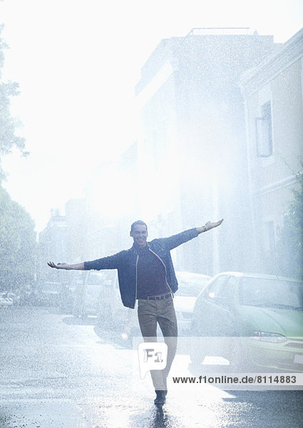 Happy man with arms outstretched in rainy street