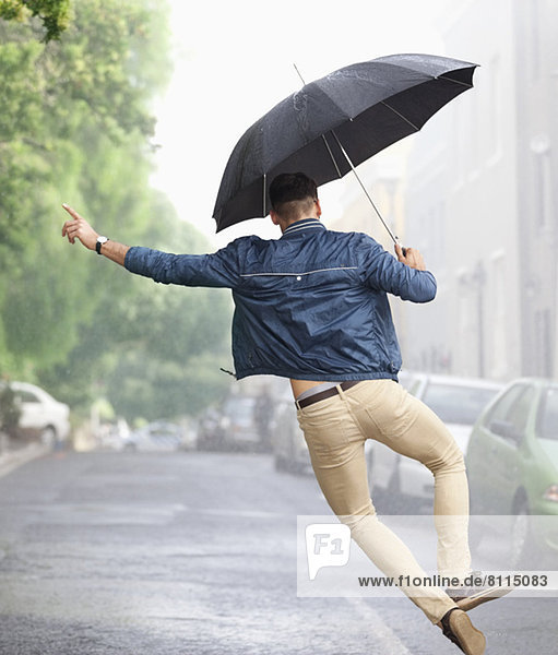 Man dancing with umbrella in rainy street