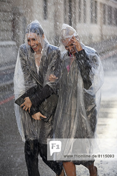 Businesswomen in ponchos walking in rainy street
