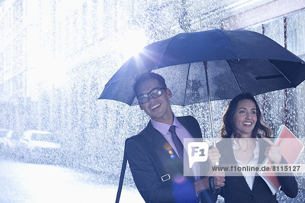 Happy businessman and businesswoman walking under umbrella in rain