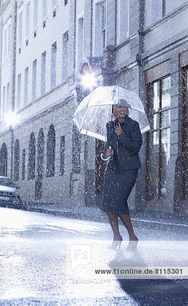 Geschäftsfrau unter dem Schirm in der verregneten Straße