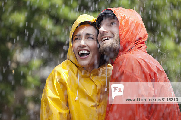Glückliches Paar in Regenmänteln schaut auf den Regen.