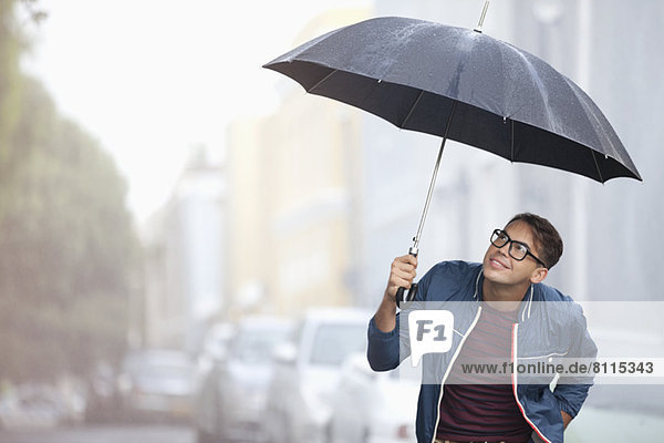 Man with umbrella looking up at rain in street