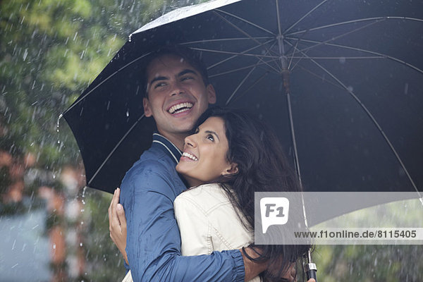 Happy couple hugging under umbrella in rain
