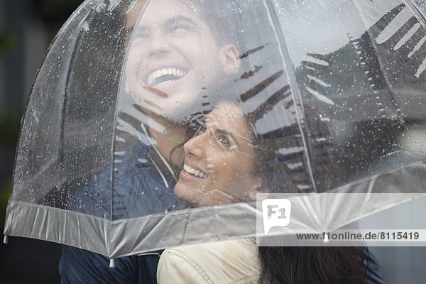 Happy couple under umbrella looking up at rain