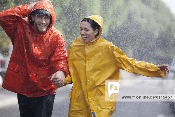 Ein glückliches Paar hält sich an den Händen und rennt in einer verregneten Straße.