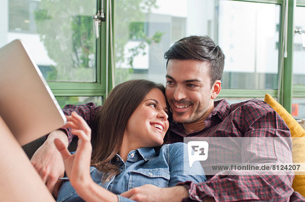 Romantisches junges Paar auf Sofa mit digitalem Tablett