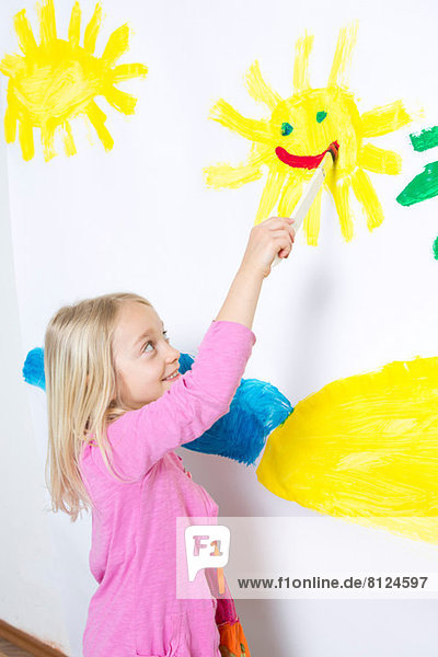 Junges Mädchen malt lächelnden Sonnenschein an die Wand