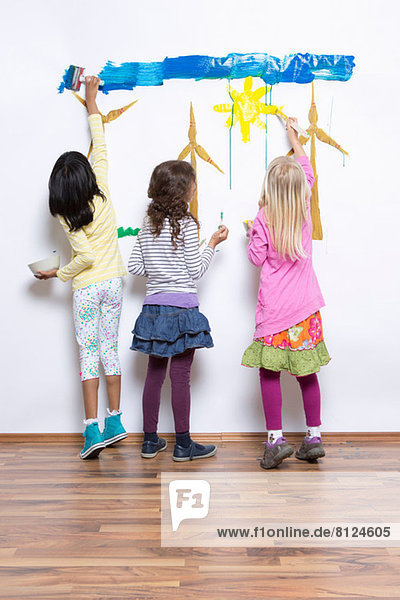 Three girls painting wind turbines on wall