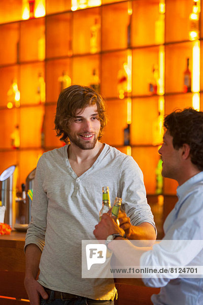 Two men standing at bar with bottles of beer