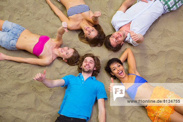 Luftaufnahme von Freunden  die mit Köpfen zusammen auf Sand liegen