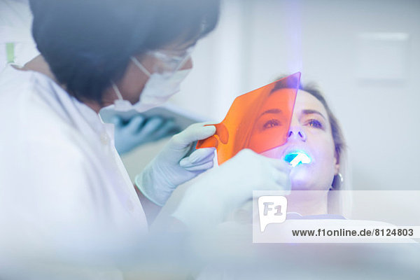 Zahnärztin mit ultraviolettem Licht an den Zähnen des Patienten