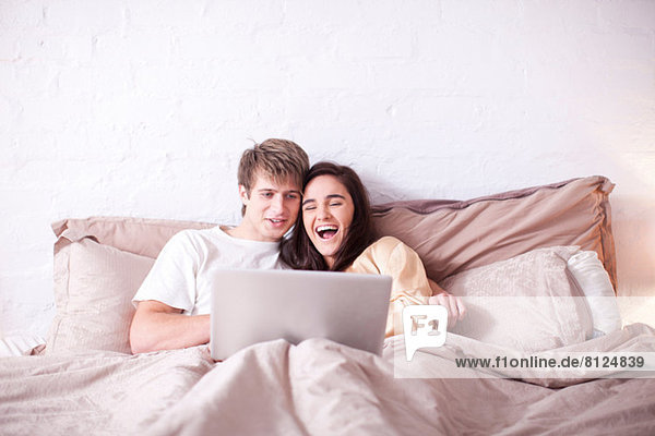 Young couple watching laptop in bed