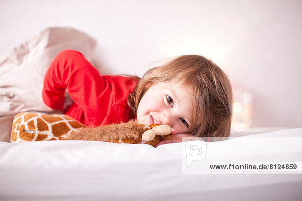Young girl lying on bed with toy giraffe