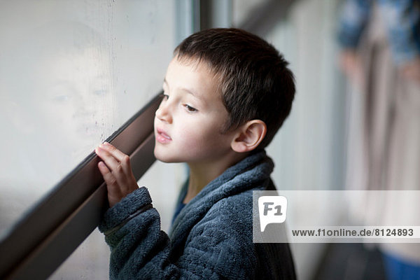 Kleiner Junge  der durch das Verandafenster schaut.