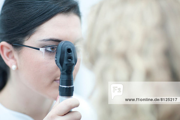 Female optician looking through ophthalmoscope