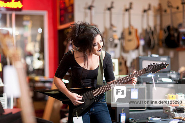 Young woman playing electric guitar in music store