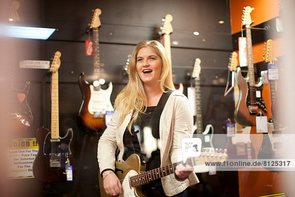 Junge Frau testet Gitarre im Musikgeschäft