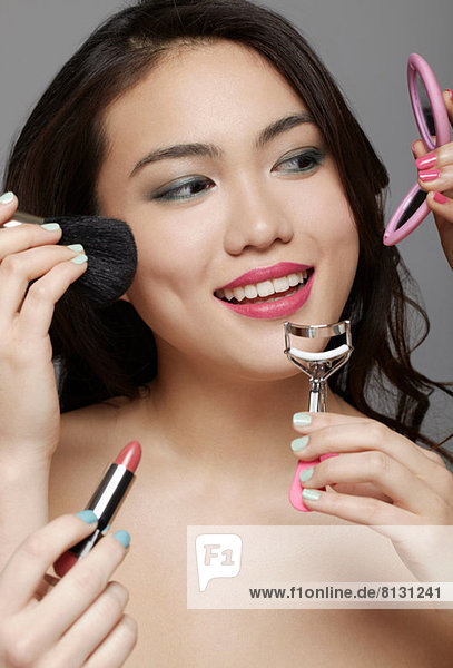 Close up of woman's face surrounded by hands holding make up and beauty equipment