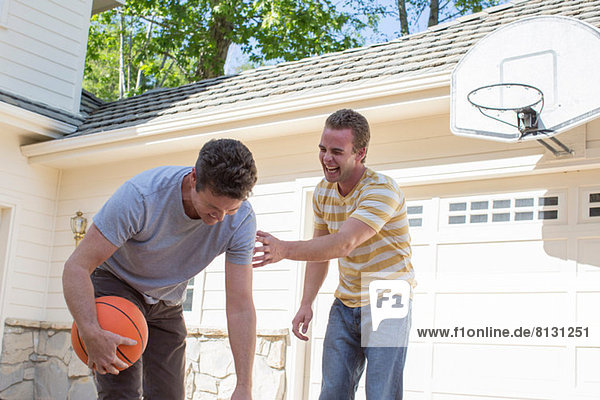 Father holding basketball with adult son laughing
