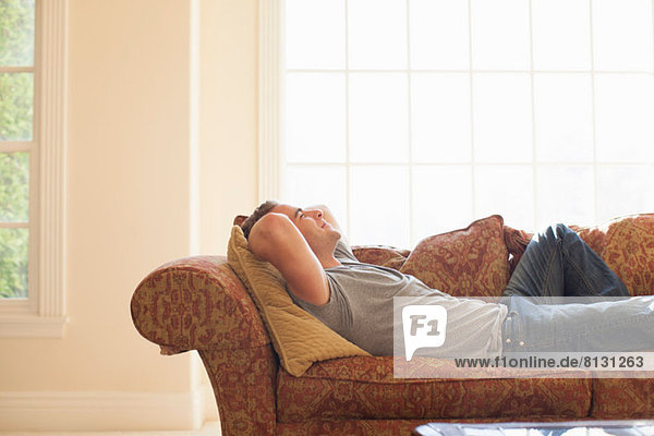 Young man lying on sofa with hands behind head