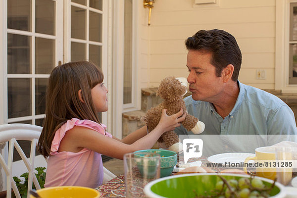 Young girl holding teddy bear for father to kiss