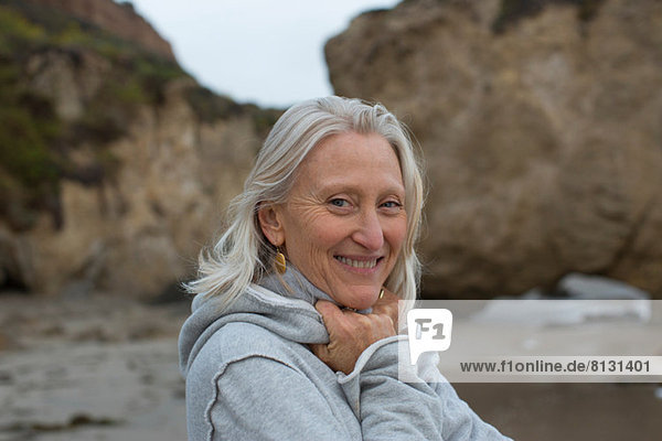 Reife Frau im grauen Pullover am Strand  lächelnd