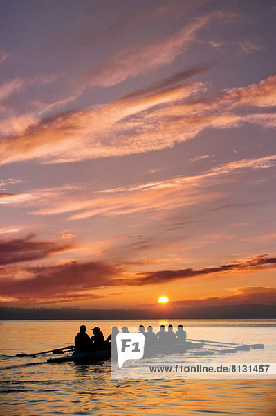 Acht Personen rudern bei Sonnenuntergang