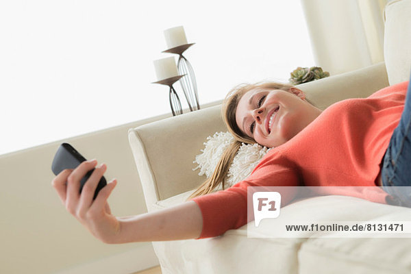 Teenagermädchen auf Sofa mit Handy  lächelnd
