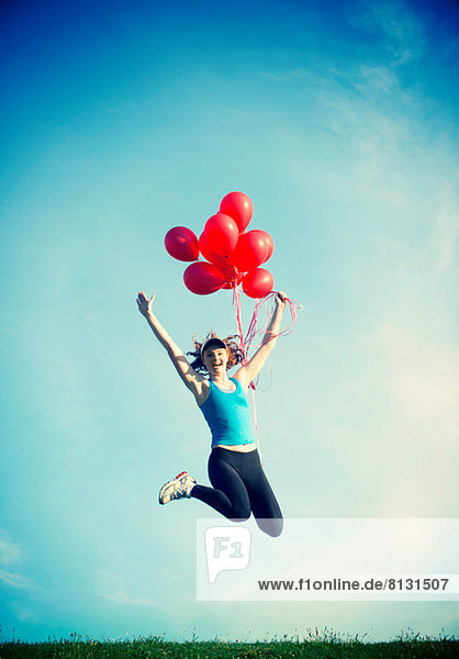 Teenager-Mädchen springt in der Luft und hält rote Luftballons.