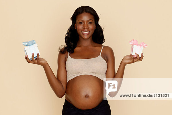 Schwangere junge Frau mit blauen und rosa Geschenkschachteln