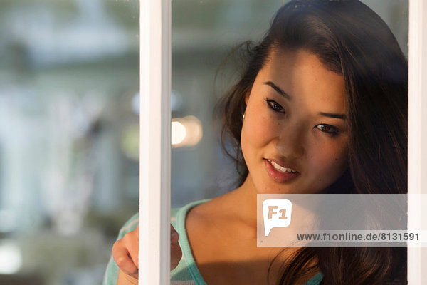 Porträt einer jungen Frau  die durchs Fenster lächelnd blickt