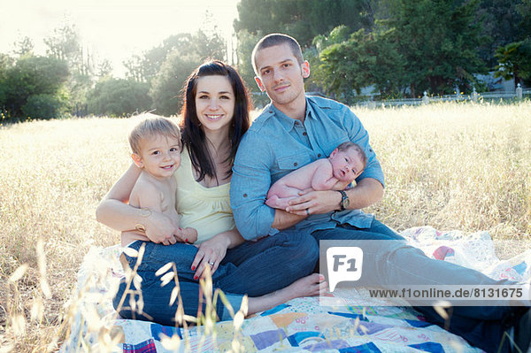 Parents with son and baby daughter on blanket in field
