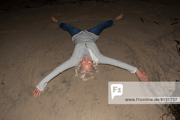 Reife Frau auf Sand liegend mit ausgestreckten Armen und Beinen