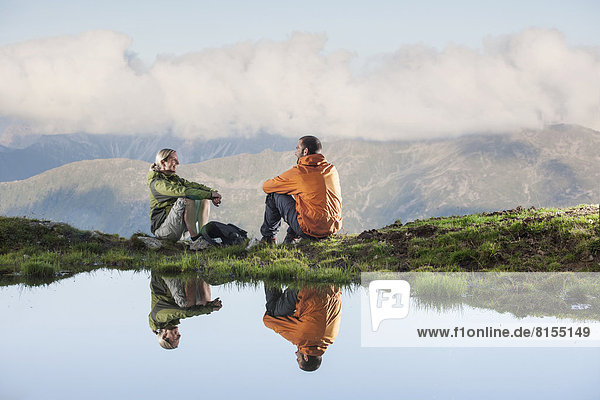Zwei Wanderer spiegeln sich in einem kleinen Bergsee