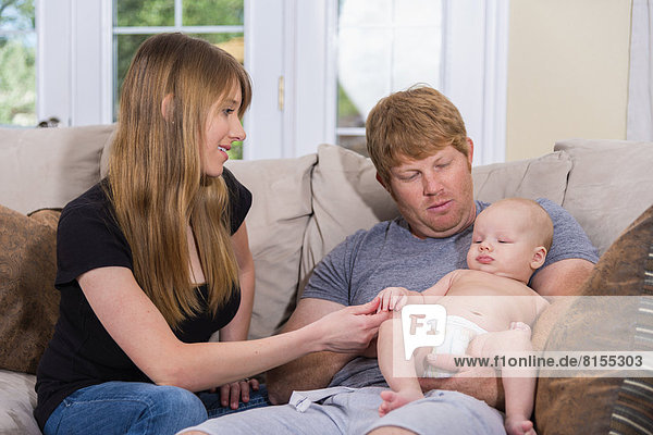 Parents with baby boy sitting on couch  smiling