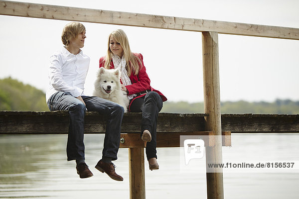 Germany  Young couple sitting on pier with dog