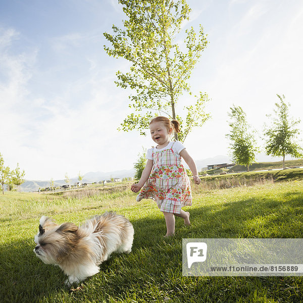 Caucasian girl chasing dog in grass