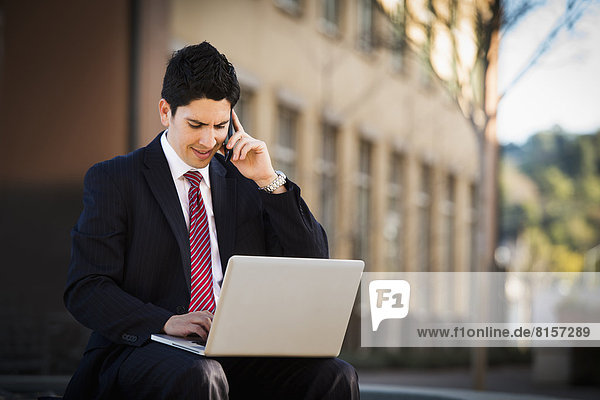 Hispanic businessman using laptop and cell phone
