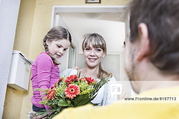 Deutschland  Nordrhein-Westfalen    Mutter und Tochter nehmen Blumen vom Briefträger  lächelnd