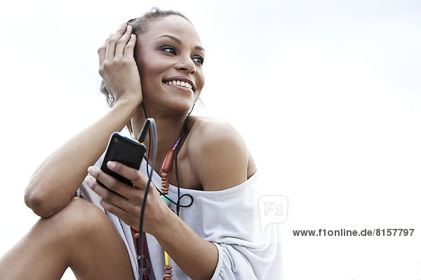Germany  Young woman listening music with head phones  smiling