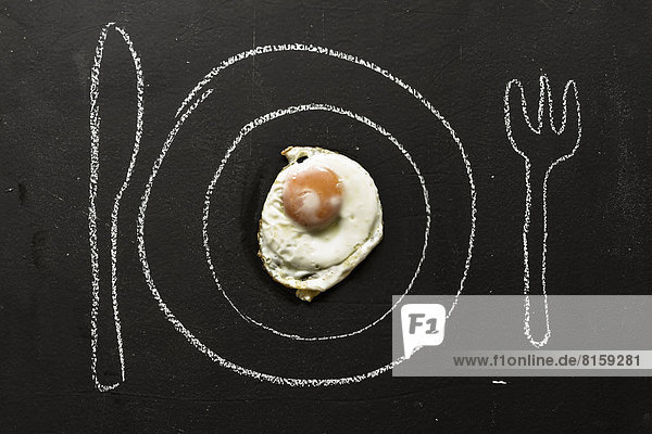 Fried egg on chalkboard with painted table setting  close up