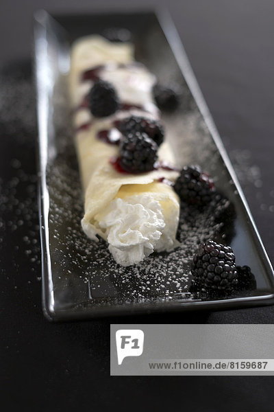 Crepes are adorned with fresh strawberries  blackberries  coulis  whipped cream  and sugar.