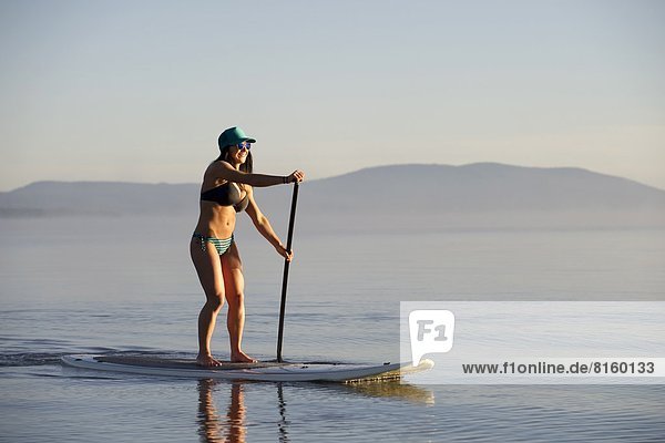 A woman  Stand Up Paddleboarding (SUP) on Lake Tahoe in the early morning on calm glassy waters  CA.