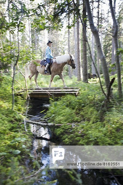 Girl horseback riding through forest